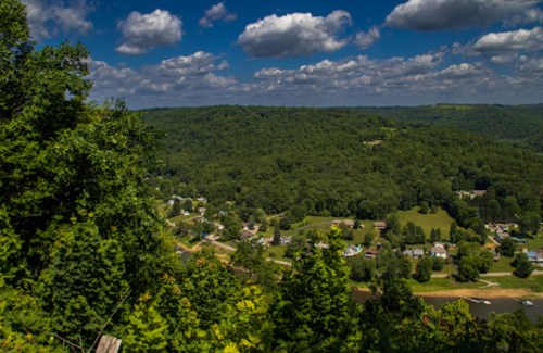 A scenic view of rolling green hills and a small town under a blue sky with fluffy clouds.