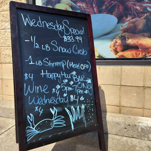 Chalkboard sign advertising Wednesday specials: $33.99 for crab, $4 wine, and happy hour from 5-7 PM.