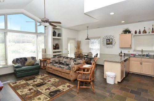 Bright, open living space with a sofa, dining area, and kitchen, featuring large windows and a cozy rug.