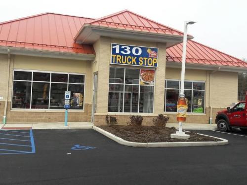 Exterior of a truck stop building with a red roof, large windows, and a sign reading "130 TRUCK STOP."