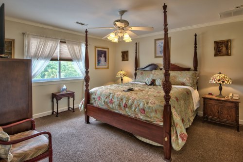 Cozy bedroom featuring a four-poster bed, floral bedding, lamps, and a window with natural light.