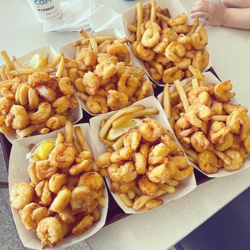 A tray filled with multiple servings of golden fried shrimp and French fries, garnished with lemon slices.