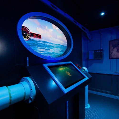 Control panel with a screen displaying ocean waves and a timer, set in a dimly lit, blue-themed room.