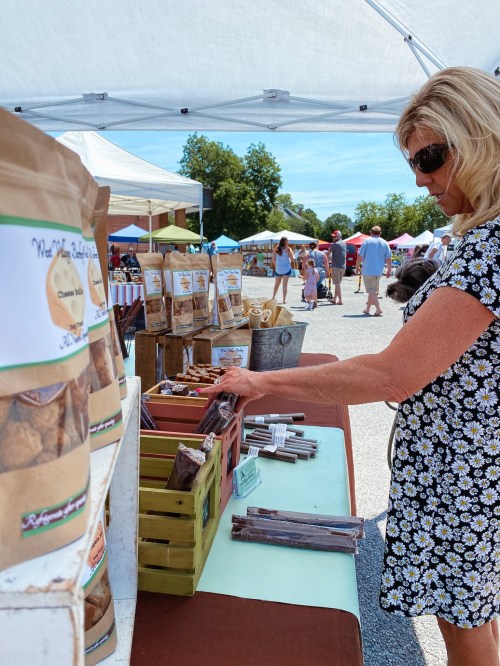 A woman browses a market stall filled with packaged goods under a tent on a sunny day.