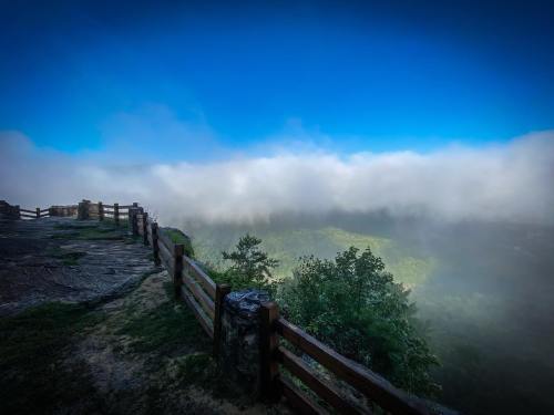 A misty landscape with a wooden fence overlooking a valley, under a bright blue sky.