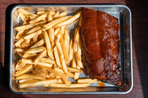 A metal tray with a large piece of glazed meat beside a generous serving of golden French fries.