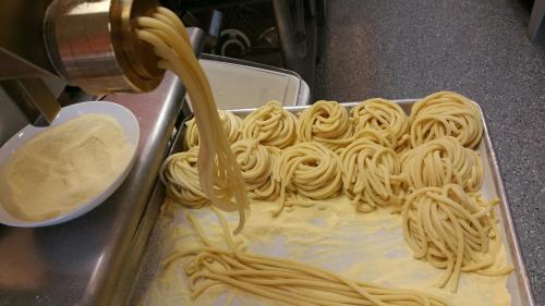 Fresh pasta being extruded from a machine onto a tray, with flour scattered underneath.