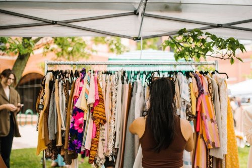 A woman browses a clothing rack filled with colorful garments at an outdoor market.