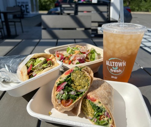 A table with two wraps, a salad, and a drink, showcasing fresh ingredients and vibrant colors in a casual setting.
