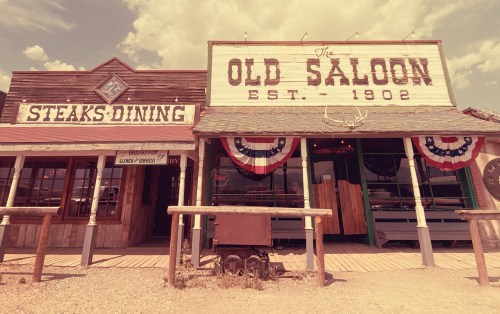 A rustic western-style building with signs for "Steaks Dining" and "The Old Saloon, Est. 1902," decorated with bunting.