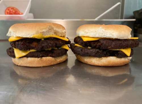 Two stacked burgers with melted cheese on a bun, resting on a stainless steel surface.