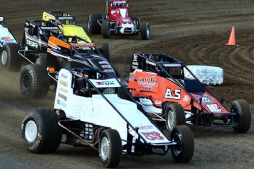 Four sprint cars race on a dirt track, kicking up dust as they compete for position in a thrilling motorsport event.