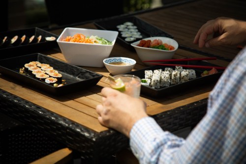 A table set with various sushi dishes, salad, and a drink, with a person’s hand holding a glass.