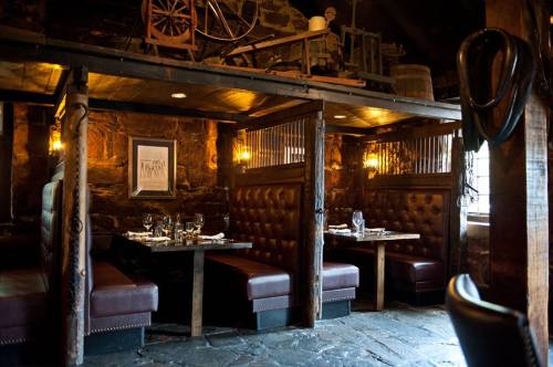Cozy restaurant interior with wooden beams, leather booths, and rustic decor, featuring dim lighting and stone walls.