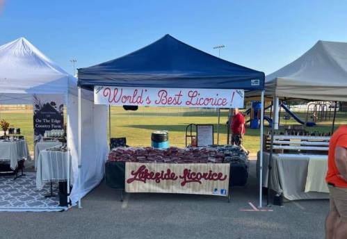 A vendor booth at an outdoor market featuring a sign that reads "World's Best Licorice" with various licorice products displayed.