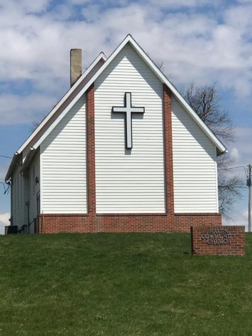 A white church building with a large cross on the side, set against a blue sky and green grass. Sign reads "Haven Community Church."