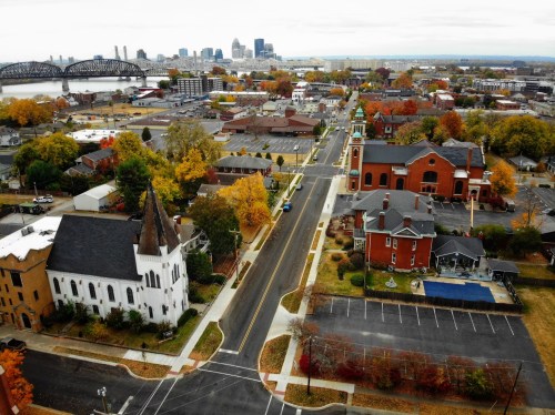 Aerial view of a cityscape with autumn trees, churches, and buildings, overlooking a river and skyline in the distance.