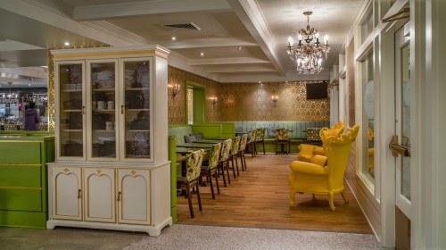 A stylish restaurant interior featuring green walls, elegant chandeliers, and yellow armchairs.