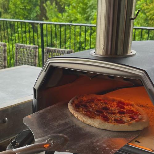 A pizza with pepperoni being pulled from a pizza oven using a metal peel.