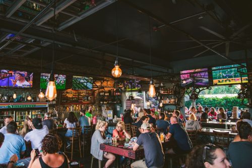 A lively bar scene with patrons enjoying drinks, watching sports on multiple screens, and a warm, inviting atmosphere.