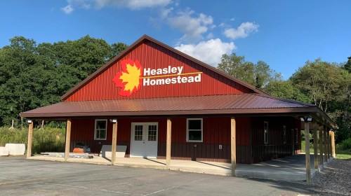 A red barn-style building with a metal roof, featuring a sign that reads "Heasley Homestead" against a blue sky.