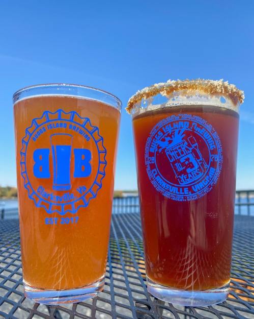Two glasses of craft beer on a table, one amber and one dark, with a scenic outdoor background.