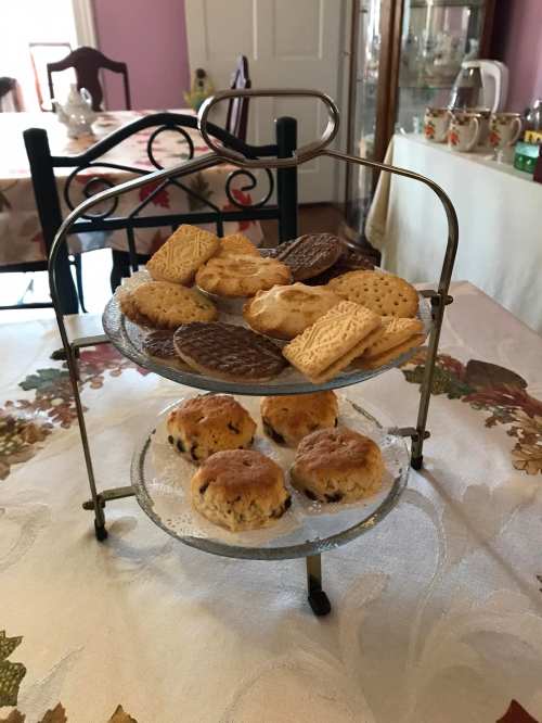 A three-tiered stand filled with various cookies and scones, set on a floral tablecloth in a cozy room.