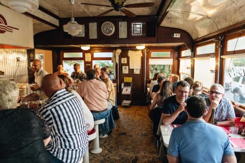 A bustling diner interior with patrons enjoying meals and conversations at tables, featuring vintage decor and warm lighting.