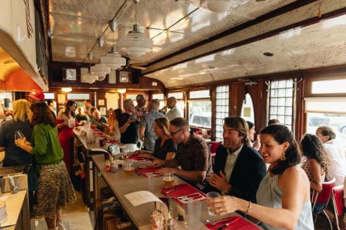 A bustling diner scene with patrons at the counter and tables, enjoying food and drinks in a lively atmosphere.