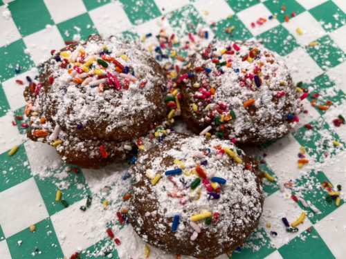 Three powdered sugar-dusted cookies topped with colorful sprinkles on a green and white checkered background.