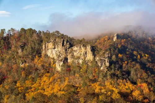 A scenic view of a rocky cliff surrounded by vibrant autumn foliage and misty mountains in the background.
