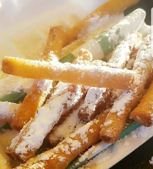 A close-up of crispy snacks dusted with powdered sugar, arranged on a plate.