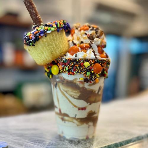 A colorful ice cream sundae topped with sprinkles, candy, and a mini cupcake on a stick.