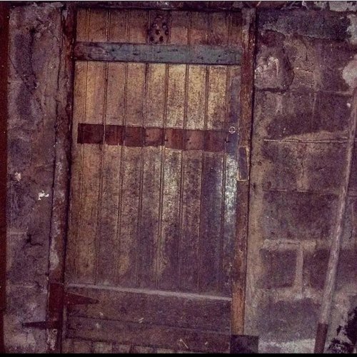A weathered wooden door with metal accents, set against a stone wall, showing signs of age and wear.