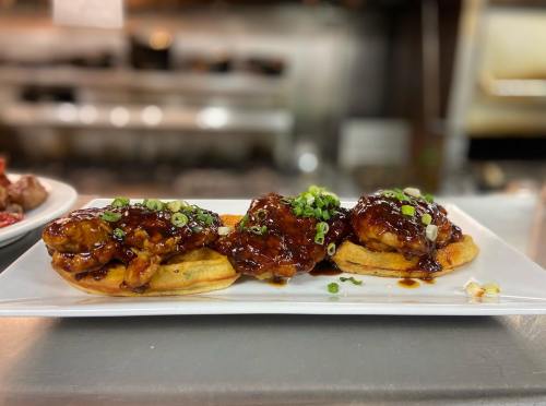 Two fried chicken pieces on waffles, topped with a rich brown sauce and garnished with chopped green onions.