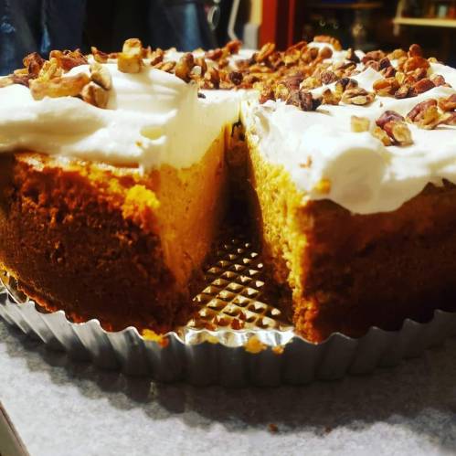 A close-up of a cake with cream frosting and chopped nuts on top, showcasing a moist, layered interior.