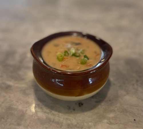 A small brown bowl filled with creamy soup, garnished with green onions, on a gray countertop.
