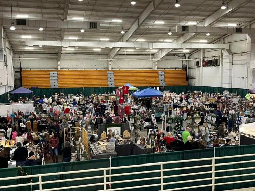 A bustling indoor market with numerous vendors and shoppers, featuring various booths and displays.