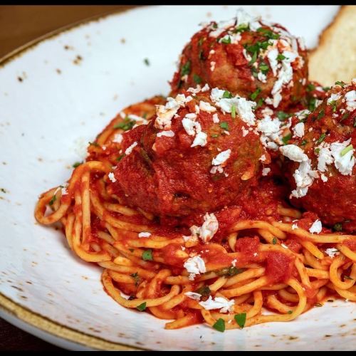 A plate of spaghetti topped with meatballs, marinara sauce, and crumbled cheese, garnished with parsley.
