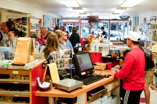 A busy shop interior with customers at the counter, chatting and browsing various items in a vibrant, welcoming atmosphere.