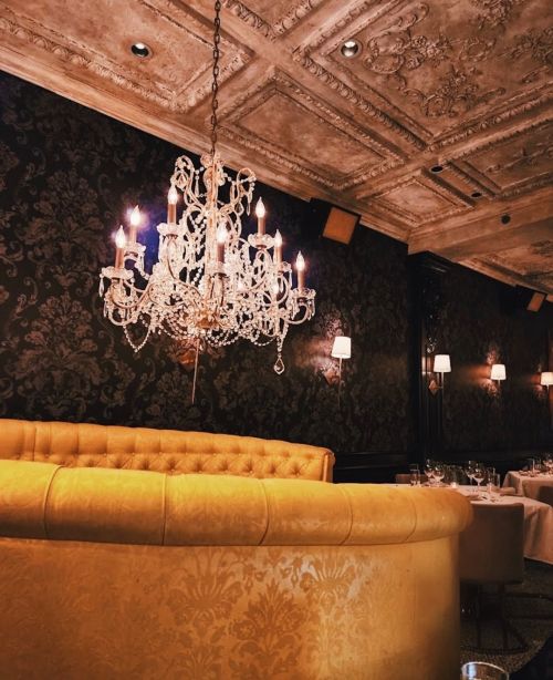 Elegant restaurant interior featuring a golden curved sofa, ornate chandelier, and dark floral wallpaper.
