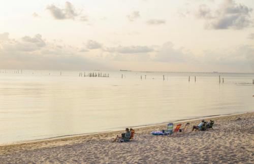 A serene beach scene at sunset with empty chairs and calm waters reflecting the sky.