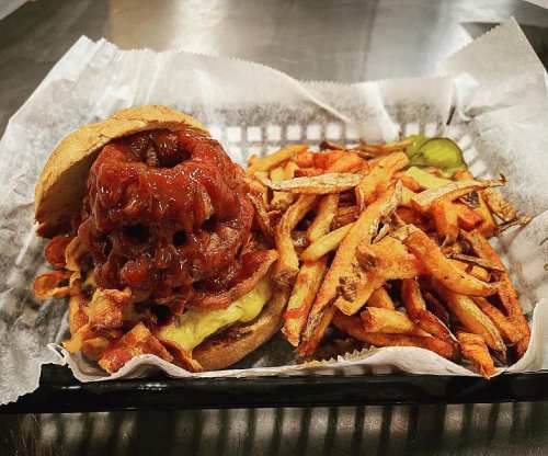 A burger topped with crispy onion rings and barbecue sauce, served with a side of golden fries in a basket.
