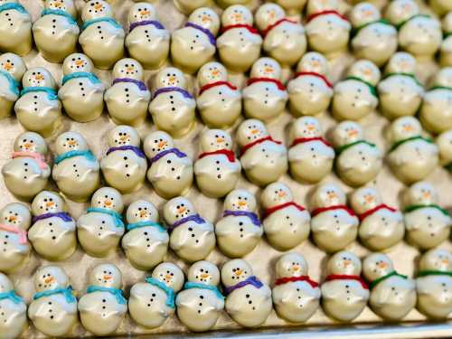 A tray filled with small, white chocolate-covered snowman treats, each decorated with colorful scarves and faces.