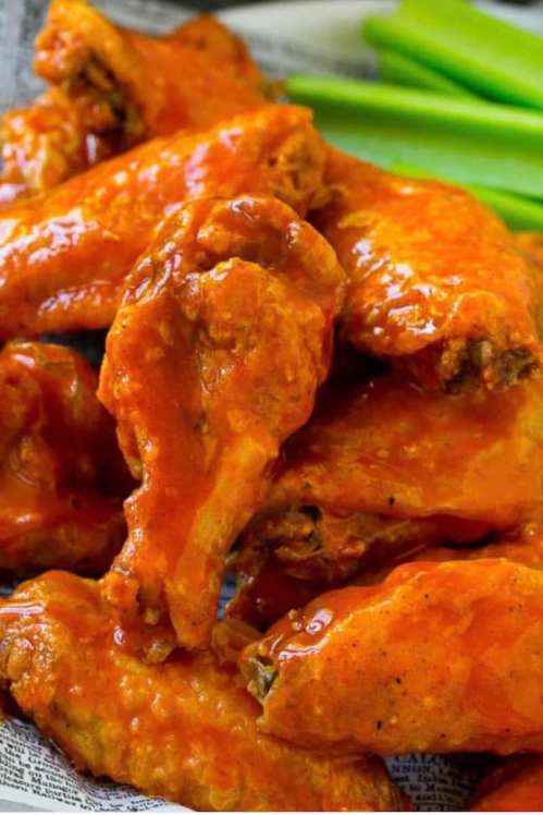 A close-up of spicy buffalo chicken wings glazed in sauce, served with celery sticks on the side.