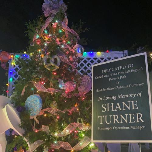 A decorated Christmas tree with lights and ornaments, featuring a dedication plaque for Shane Turner, Mississippi Operations Manager.