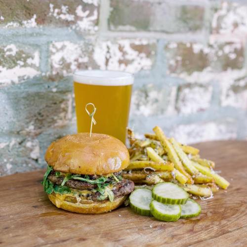 A juicy burger with lettuce, pickles, and a pint of beer, accompanied by crispy fries on a wooden table.