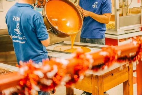 A person in a blue shirt pours caramel into a tray, with festive decorations in the foreground.