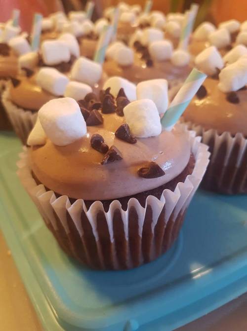 Chocolate cupcakes topped with frosting, mini marshmallows, chocolate chips, and colorful straws.