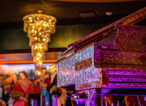 A beautifully decorated piano in a dimly lit venue, with a sparkling chandelier in the background.